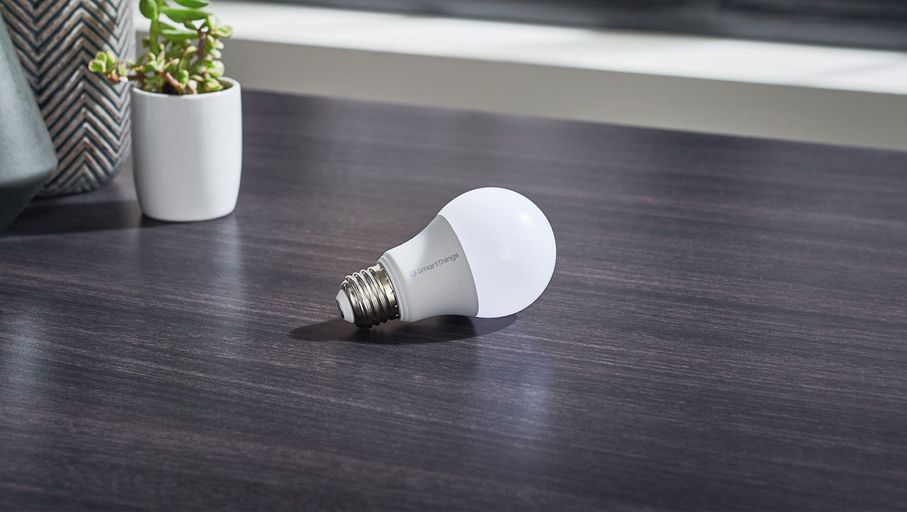  A smart bulb on a desk, with some potted plants behind it  